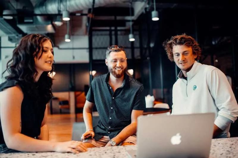 Three colleagues talking around an open MacBook in an office
